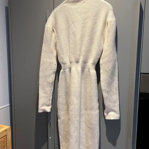 Adoore stickad långklänning st moritz - Säljer en vit stickad långklänning med polokrage och långa ärmar. Klänningen har en rak passform och är tillverkad i en mjuk blandning av akryl, polyester, nylon och ull. Perfekt för kyligare dagar och enkel att styla.