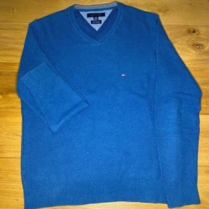 Blå tröja från Tommy Hilfiger - Säljer en snygg blå tröja från Tommy Hilfiger i bomull och kashmir. Tröjan har en v-ringad design och långa ärmar. Perfekt för en stilren look.