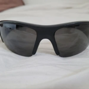 Svarta sportiga solglasögon från Nike - Snygga och sportiga svarta solglasögon från Nike med en strömlinjeformad design. Perfekta för utomhusaktiviteter med en bekväm passform och mörka linser som skyddar mot solen. Nike-loggan syns på sidan av bågarna.