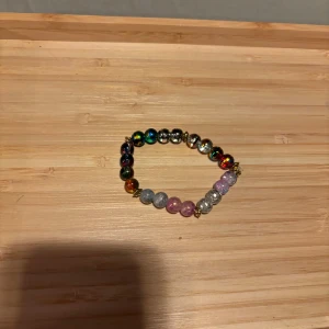 Färgglatt pärlarmband - Säljer ett färgglatt armband med pärlor i olika nyanser av rosa, blått, silver och flerfärgat. Perfekt för att ge en färgklick till din outfit. Armbandet är elastiskt och passar de flesta handleder.