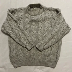 Beige stickad tröja med flätmönster - Säljer en mysig beige stickad tröja med flätmönster. Tröjan har en rund hals och långa ärmar med ribbade muddar. Perfekt för när vintern kommer tillbaka. Köpt second hand men inga tecken på användning 