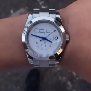 Snygg och rolig klocka med texten 'Who cares I'm already late' på urtavlan. Klockan har en silverfärgad metallarmband och blå visare. Perfekt för den som vill ha en humoristisk touch på sin stil.