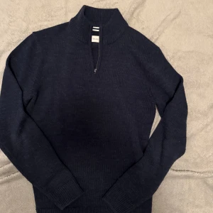 Mörkblå stickad tröja  - Säljer en stilren mörkblå stickad tröja från Peak Performance. Tröjan har en dragkedja vid halsen och långa ärmar med ribbade muddar. Perfekt för kyliga dagar!
