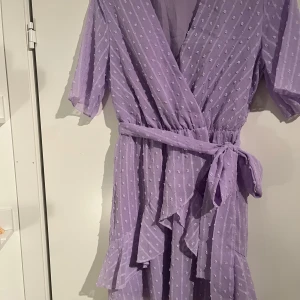Lila omlottklänning - Säljer en söt lila omlottklänning från Shein med knytband i midjan och volangdetaljer. Perfekt för vår och sommar! Storlek S, aldrig använd!
