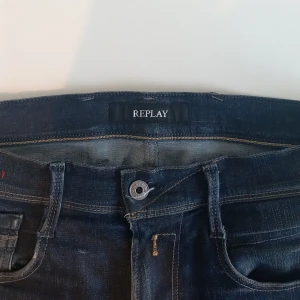 Mörkblå jeans från Replay - Snygga mörkblå jeans från Replay med klassisk femficksdesign och knappgylf. Perfekta för en avslappnad stil. Märkesdetaljer syns på fickan och baksidan.