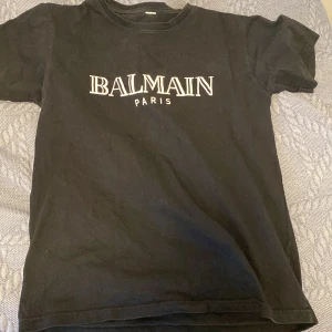 Svart t-shirt från Balmain - Säljer en svart t-shirt från Balmain med vit text på bröstet. T-shirten har en klassisk rund hals och korta ärmar. Perfekt för en stilren och avslappnad look. Pris går att diskutera! OBS 1 till I 
