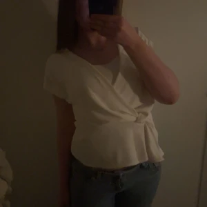 Vit omlottopp - Säljer en stilren vit omlottopp med korta ärmar. Toppen har en elegant knytdetalj i midjan som ger en fin passform. Perfekt för en avslappnad men chic look. Pris kan diskuteras 