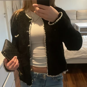 Svart cardigan  - Snygg svart cardigan jacka från CC-company med vita detaljer och knappar. Jackan har en klassisk design med långärmade ärmar och en normal passform. Perfekt för att ge en stilren touch till din outfit. Nypris 499kr, säljer för 139kr. 