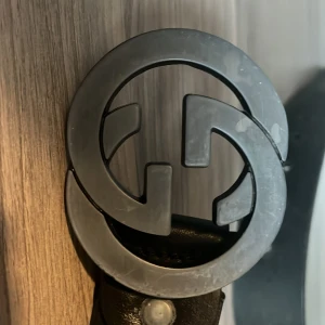 Svart bälte med GG-spänne - Snyggt svart bälte med ett stort GG-spänne i silver. Bältet har en grön och röd randig detalj längs med remmen. Perfekt för att ge en stilren touch till din outfit.