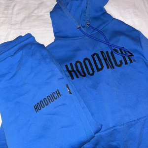 Blå hoodie från Hoodrich - Snygg blå hoodie från Hoodrich med svart logotyp på bröstet. Perfekt för en avslappnad stil. Hoodien har en klassisk design med dragsko i huvan och ribbade muddar vid ärmslut och nederkant. storlek xs på tröja och s på byxa