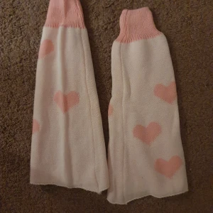 Vita benvärmare med rosa hjärtan - Säljer ett par mysiga vita benvärmare med söta rosa hjärtan. De har en bred ribbad kant upptill i rosa som håller dem på plats. 