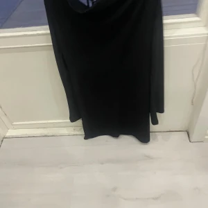 Svart långärmad klänning - Elegant svart klänning med långa ärmar och en stilren design. Klänningen har en öppen rygg med snörning som ger en extra touch av stil. Perfekt för en kväll ute eller en speciell tillställning.