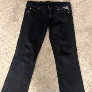 Svarta jeans från Replay - Snygga svarta jeans från Replay med klassisk femficksdesign och knappgylf. Jeansen har en stilren look och är perfekta för en avslappnad stil. Märkesdetaljer syns på fickan och baksidan.
