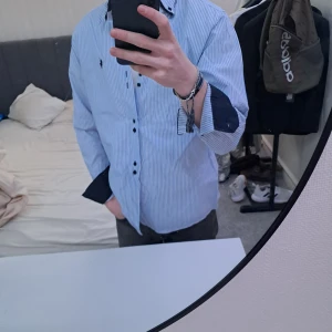 Blå och vit randig skjorta från Ralph Lauren - Säljer en stilren blå och vit randig skjorta från Ralph Lauren. Skjortan har långa ärmar och blåa knappar som ger en snygg kontrast. Perfekt för en klassisk look.