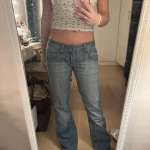 Blå jeans från Fishbone - Säljer ett par snygga blå jeans från Fishbone. De har en bootcut-stil och är lågmidjade med knappar på bakfickorna. Perfekta för en avslappnad look. Midjemått 38 innerben 78