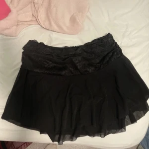 Minikjol - Snygg svart kortkjol med spetsdetaljer i midjan. Kjolen har en luftig passform och är perfekt för en stilren look. Den är enkel att matcha med olika toppar och accessoarer.