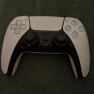 Vit och svart spelkontroll - Säljer en vit och svart spelkontroll för PlayStation. Den har en modern design med två analoga spakar, styrkors och flera knappar för en optimal spelupplevelse. Perfekt för gamingkvällar eller som extra kontroll. 🎮