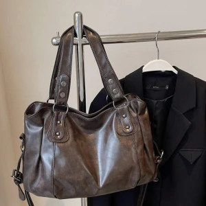 Brun axelväska i syntet - Snygg brun axelväska i syntetmaterial med dubbla handtag och dragkedja. Perfekt för att bära med sig det nödvändigaste. Väskan har en stilren design med metallnitar som detaljer. Nytt skick ej använd och säljer pga jag ej använder den och passar ej min stil