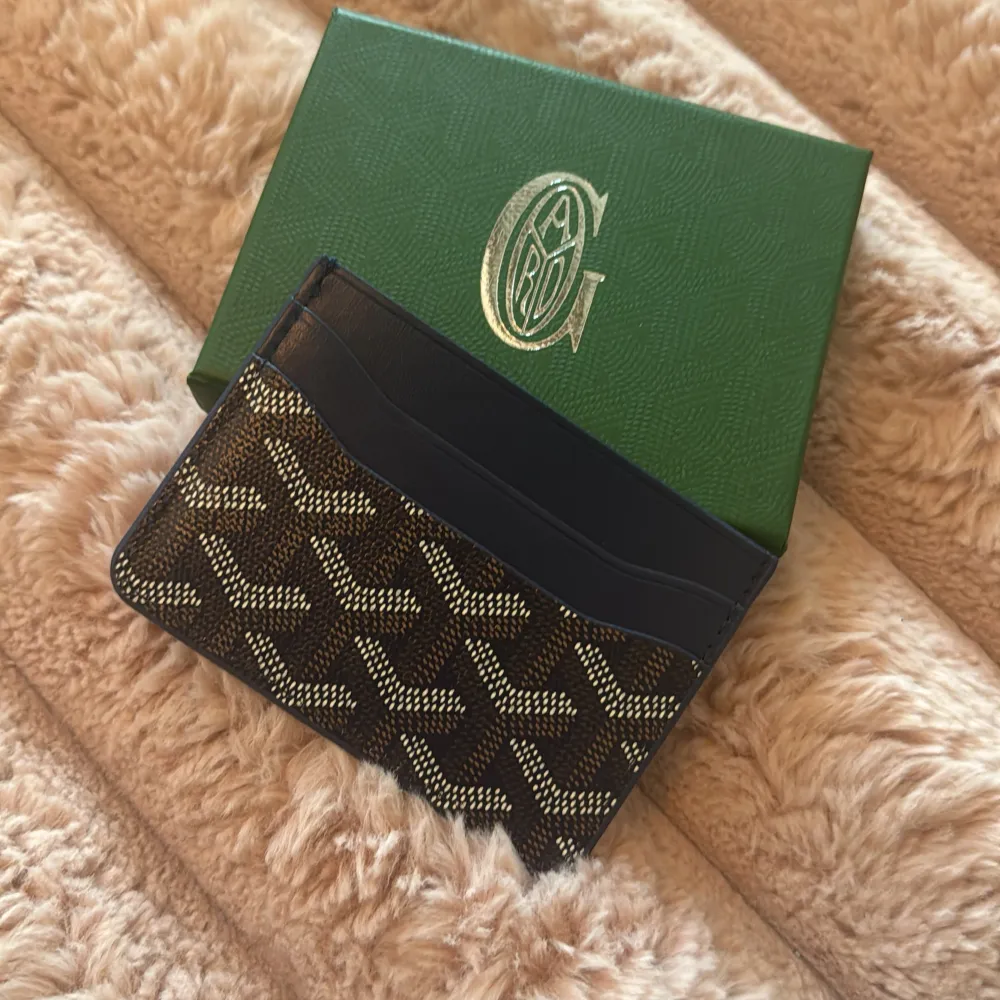 Snygg och stilren korthållare med ett ikoniskt mönster. Perfekt för att hålla dina kort organiserade med stil. Kommer i en elegant grön förpackning.. Asusteet.