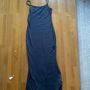 Svart långklänning med smala axelband - Elegant svart långklänning med smala axelband. Perfekt för en stilren och minimalistisk look. Klänningen har en enkel design som gör den lätt att matcha med olika accessoarer.