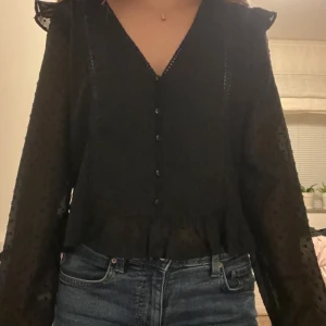 Svart blus med spetsdetaljer - Säljer en svart blus med fina detaljer. Fina volanger på sidorna. 