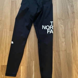 Svarta leggings från The North Face - Snygga svarta leggings från The North Face med logga på benet. Perfekta för både träning och vardag. De har en tight passform och är tillverkade i ett stretchigt material för bästa komfort.