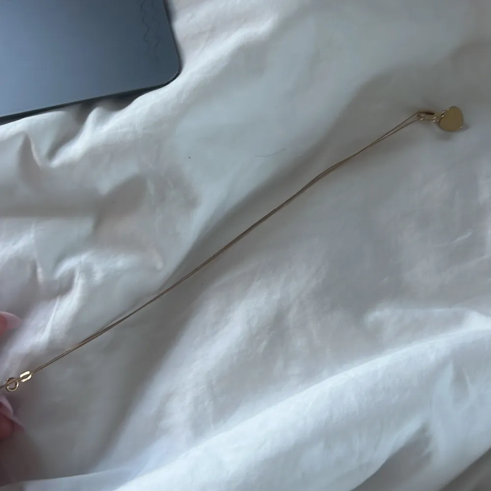 Elegant guldhalsband med ett litet hjärthänge. Perfekt för att lägga till en subtil touch av kärlek och stil till din outfit. Kedjan är tunn och smidig, brickan har inget inskrivet på sig . Asusteet.