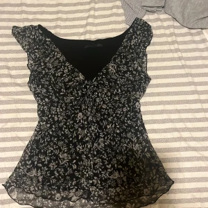 Svart blommig blus från H&M - Säljer en elegant svart blus från H&M med ett vackert blommönster i vitt. Blusen har korta ärmar och en lätt v-ringad design. Perfekt för en stilren look. Det står 46 men passar jättebra på storlek M-L då jag haft på mig den och satt inte för hårt eller för pösigt 