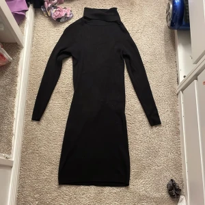 Svart ribbad klänning med polokrage - Snygg svart ribbad klänning med polokrage och långa ärmar. Perfekt för kyligare dagar och kan stylas upp eller ner beroende på tillfälle. Klänningen har en tight passform som framhäver figuren.