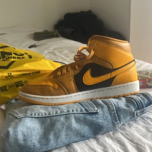 Nike Air Jordans i gult och svart - Snygga Nike Air Jordans i en iögonfallande gul och svart färgkombination. Skorna har klassisk snörning och en vit sula som kontrasterar snyggt mot det färgglada överdelen. Perfekta för att ge din outfit en sportig touch.