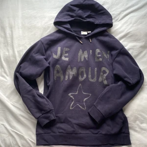 Sötaste, mysigaste hoodien🩷🩷 - Säljer en mörkblå hoodie från Gina Tricot med texten 'Je m'en amour' och en stjärna på framsidan, i glitter text. Tröjan har en klassisk huva och långa ärmar!💕