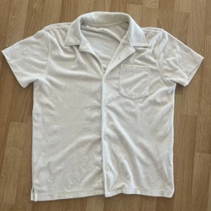 Vit frotté skjorta  - Säljer en vit kortärmad frotte skjorta med knappar och en bröstficka. Riktigt snygg och bekväm till sommaren. Skriv vid funderingar!