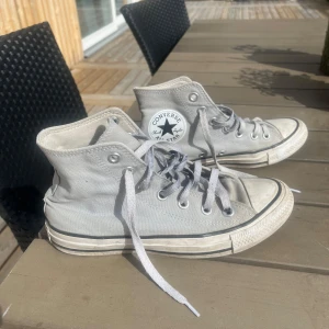 Gråa höga Converse - Säljer ett par klassiska gråa höga Converse sneakers med snörning. Skorna har används en del men skulle säga att de är i bra skick! 