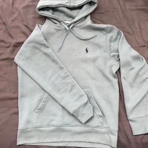 hoodie från Ralph Lauren - Snygg ljusgrön hoodie från Ralph Lauren med klassisk broderad logga på bröstet. Tröjan har en känguruficka och justerbar huva med dragsko. Perfekt för en avslappnad stil. Helt oanvänd på grund av att den är för liten