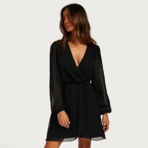 Svart klänning - Snygg omlottklänning från Nelly i storlek 34 med volang. Några få lösa trådar vid slutet av v-ringningen men annars är den i bra skick💋🖤