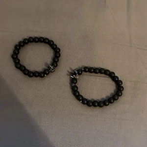 Svarta pärlarmband med dödskalle och krona - Två stilrena svarta pärlarmband med detaljer i form av en dödskalle och en krona. Perfekta för att ge en edgy touch till din outfit. Elastiska och bekväma att bära.