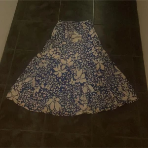 Blommig kjol från Lindex - Säljer en blå och vit blommig kjol från Lindex i storlek XS. Kjolen har ett vackert blommönster och är perfekt för en somrig look. Den är luftig och bekväm, vilket gör den idealisk för varma dagar. Passar bra till både vardag och speciella tillfällen.