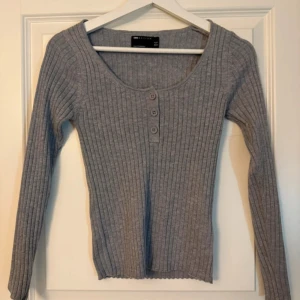 Grå ribbad tröja från ASOS DESIGN - Säljer en stilren grå ribbad tröja från ASOS DESIGN. Tröjan har en rund halsringning med tre knappar framtill och långa ärmar. Perfekt för en avslappnad look.