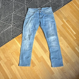 Blå jeans från Nudie Jeans - Säljer ett par snygga blå jeans från Nudie Jeans. De har en klassisk femficksdesign och en normal passform. Jeansen är tillverkade i slitstarkt denim och har en stilren ljusblå tvätt. Perfekta för en avslappnad look! Inga skador och PRIS KAN DISKUTERAS!