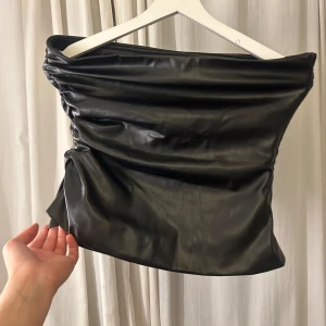 Svart tubtopp - Svart tubtopp i skinnimitation med en stilren och modern design. Toppen har en tight passform och är perfekt för att ge en edgy touch till din outfit. Använd 1 gång.