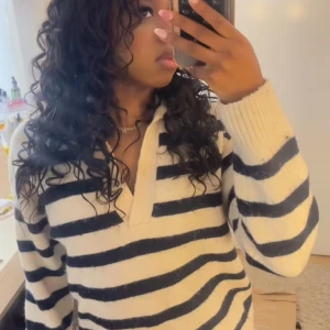 Randig stickad tröja - Säljer en mysig stickad tröja med breda svarta och vita ränder. Tröjan har en v-ringad design och långa ärmar, perfekt för kyligare dagar. Den är både stilren och bekväm.