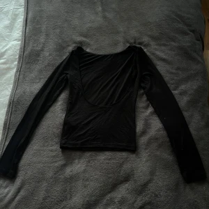 Svart långärmad topp - Säljer en stilren svart långärmad topp med djup urringning från Gina. Perfekt för en elegant look. Passar bra till allt. Aldrig använt pga för stor för mig. Storlek S