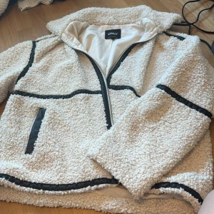 Vit teddyjacka från ONLY - Mysig vit teddyjacka från ONLY med svarta detaljer och dragkedja. Jackan har en avslappnad passform och är perfekt för kyligare dagar. Den har långa ärmar och praktiska fickor framtill. Endast använd en höst och i bra skick💕passar även storlek s