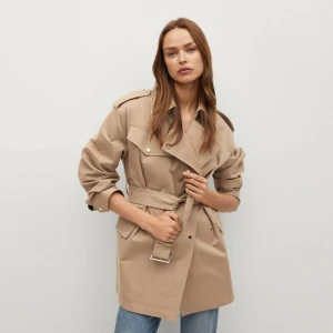 Beige trenchcoat från Mango - Snygg beige trenchcoat från Mango med klassisk design. Jackan har ett bälte i midjan och knappar framtill. Perfekt för vår och höst. Den har långa ärmar och en stilren look.