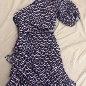 Mönstrad klänning från Mango - Snygg mönstrad klänning från Mango i marinblått med små blommor i rosa och beige. Klänningen har en oneshoulder-design och volangdetaljer. Perfekt för sommaren! Det står 36 på prislappen men jag skulle uppskatta den som mer av en 34 eller eventuellt 32.