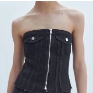 Svart jeanskorsett med dragkedja Zara - Snygg svart korsett i jeansmaterial med dragkedja framtill och dekorativa ficklock med knappar. Perfekt för en trendig look. Tyvärr tappat den man drar upp med men inget man tänker på