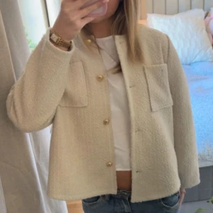 Beige jacka från Cortefiel - Säljer en stilren beige jacka från Cortefiel. Jackan har en normal passform med långa ärmar och knappar framtill. Den är tillverkad i ett strukturerat material och har två framfickor med knappar. Det står att den är i XL men absolut inte mer som en S