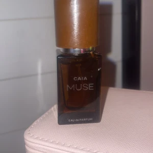 CAIA Muse Eau de Parfum - Säljer en elegant flaska av CAIA Muse Eau de Parfum. Flaskan är brun med en stilren design och har en kapacitet på 15 ml. Parfymen är skapad i Paris och tillverkad i Stockholm, vilket ger en känsla av lyx och internationell flair.