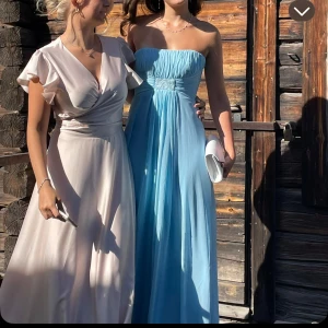 Ljusblå balklänning  - Elegant ljusblå axelbandslös långklänning med draperad överdel och markerad midja med korsett. Perfekt för formella bland annat balen. Bara använd en gång och varit på kemtvätt efter det. Köptes för 1200kr. Finns tunna axelband till. 