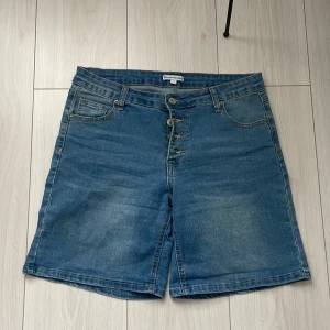 Blå jeansshorts från Sincerely Love - Snygga blå jeansshorts från Sincerely Love med klassisk femficksdesign och knappar framtill. Perfekta för en avslappnad stil under varma dagar. De har en normal passform och är tillverkade i slitstarkt denim.